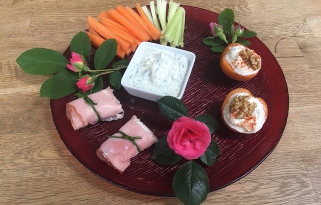 Teller mit Schinken-Käse-Röllchen, Marillen-Käse-Happen, Karotten- und Selleriesticks mit Dip; geschmückt mit Rosenblüten und -blättern