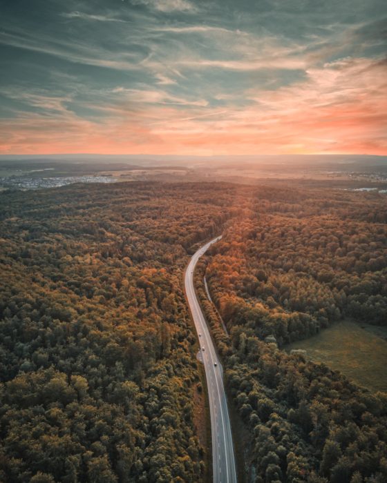Luftbild einer Straße durch Wald, im Hintergrund der Horizont in der Abenddämmerung