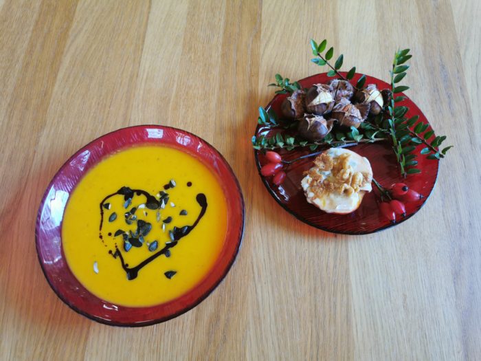 2 rote Teller, einer mit Kürbiscremesuppe mit gehackten Kürbiskernen und Kernöl, einer mit Maroni und einem gebratenen Apfel mit Gorgonzola und Walnüssen