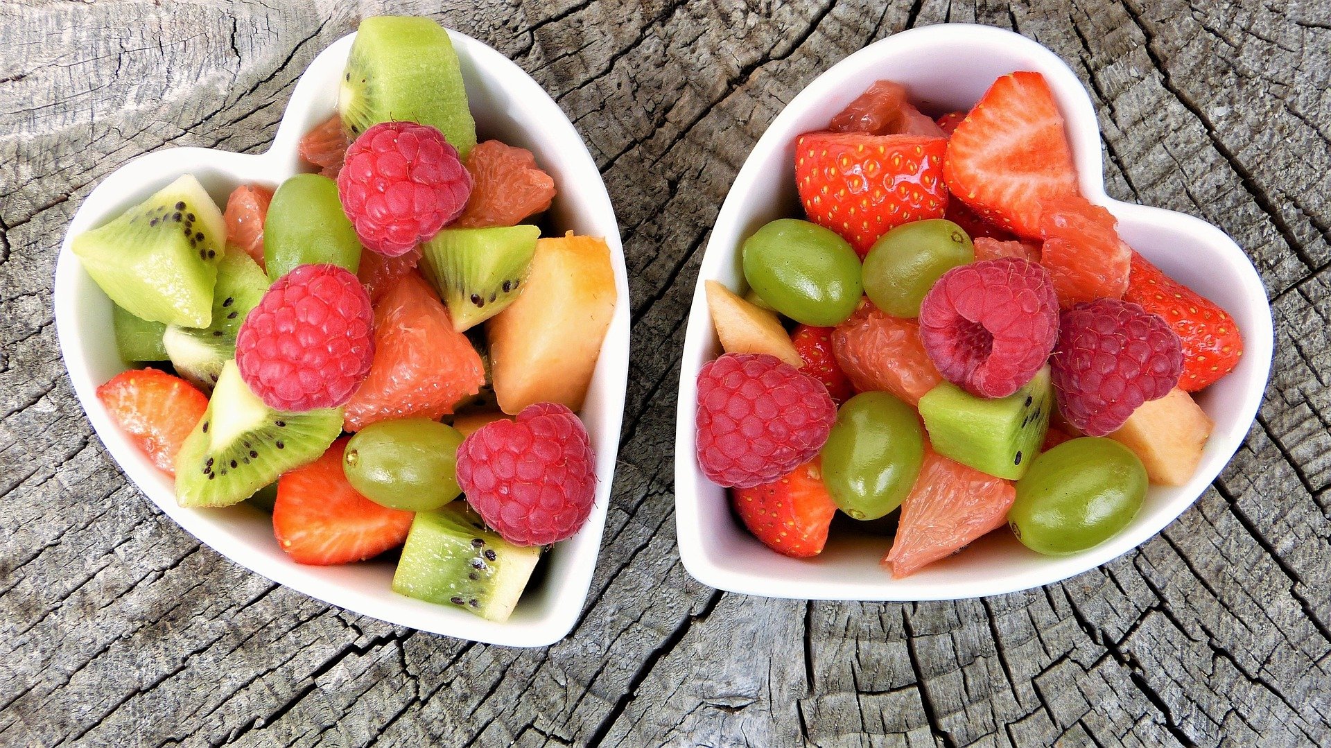 gemischtes Obst in zwei herzförmigen Schüsseln angerichtet, auf einem Baumstamm platziert