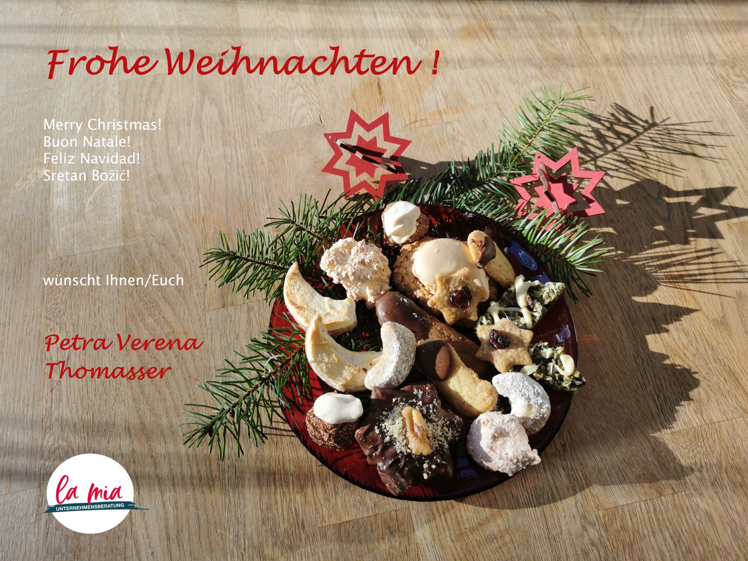 roter Teller voll Weihnachtskeksen, Fichtenzweige und rote Sterne als Deko, Weihnachtswünsche von Petra Verena Thomasser, la mia Unternehmensberatung-Logo